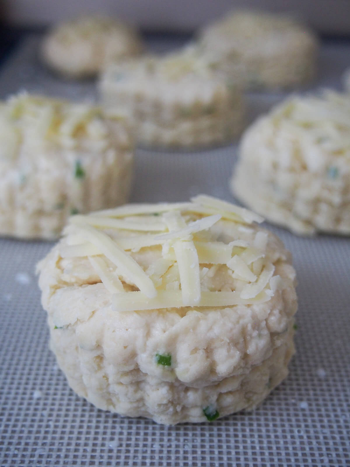 cheese scones topped with cheese before baking in oven raw cheese scones on baking sheet before baking with some extra cheese on top