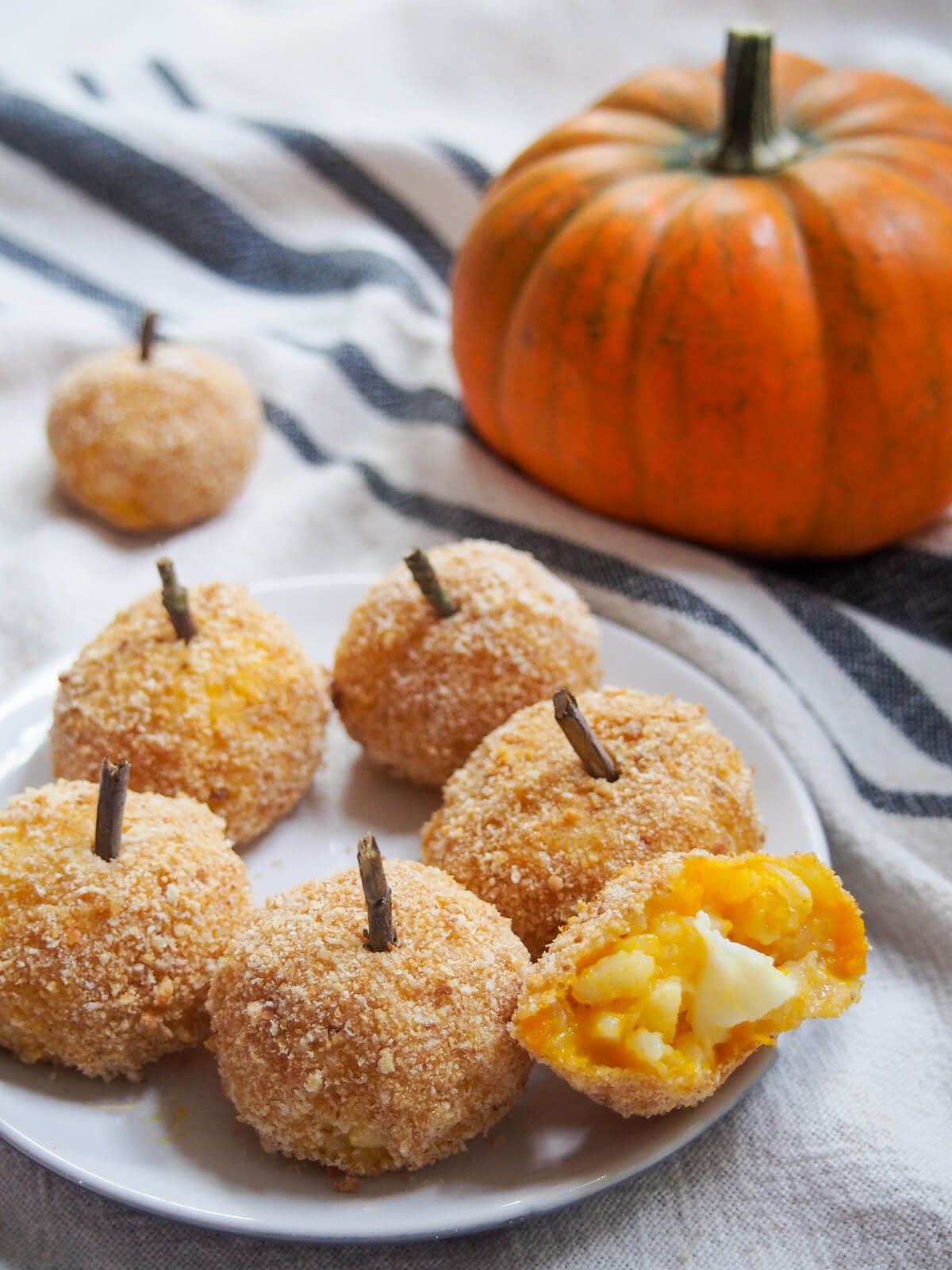 plate of pumpkin arancini with one bitten into on side and pumpkin behind