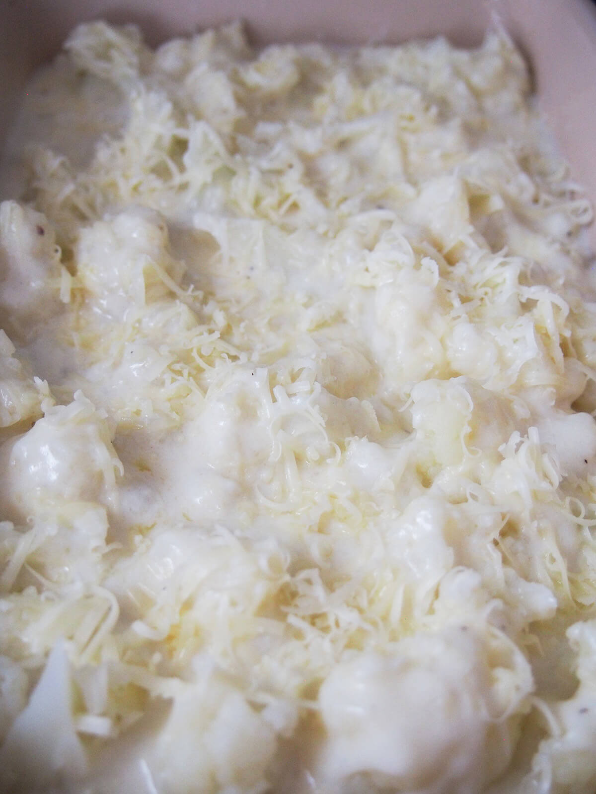 cauliflower cheese before baking cauliflower topped with cheese sauce with grated cheddar on top