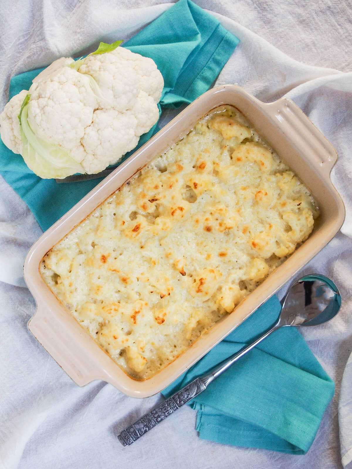 Cauliflower cheese is a classic British side dish that pairs perfectly with a roast, but also with a range of other dishes. It's easy, tasty and wonderfully comforting. dish of cauliflower cheese with part caulifower to one side and serving spoon on other