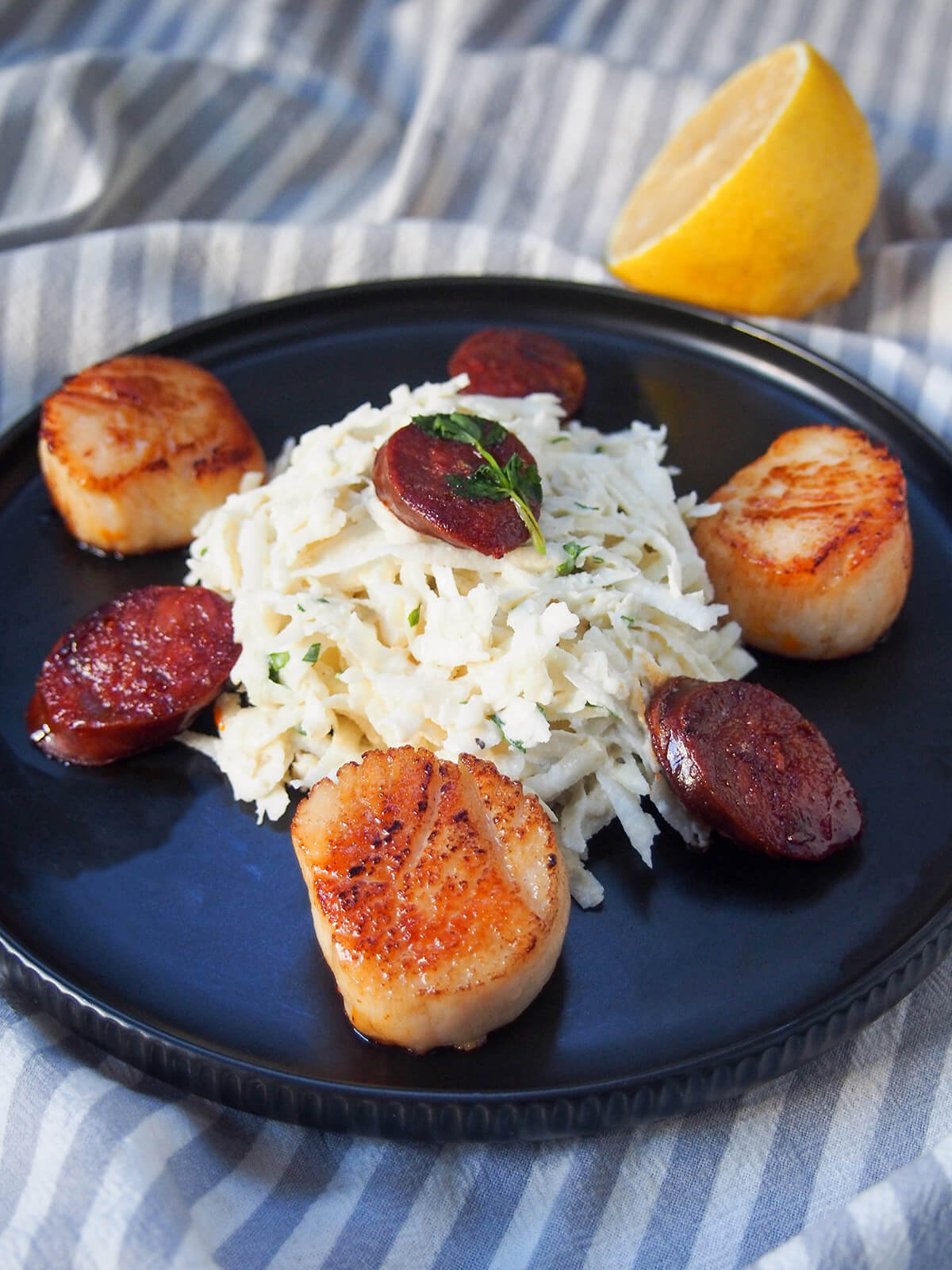 plate of celeriac remoulade seared scallops and chorizo with cut lemon behind plate