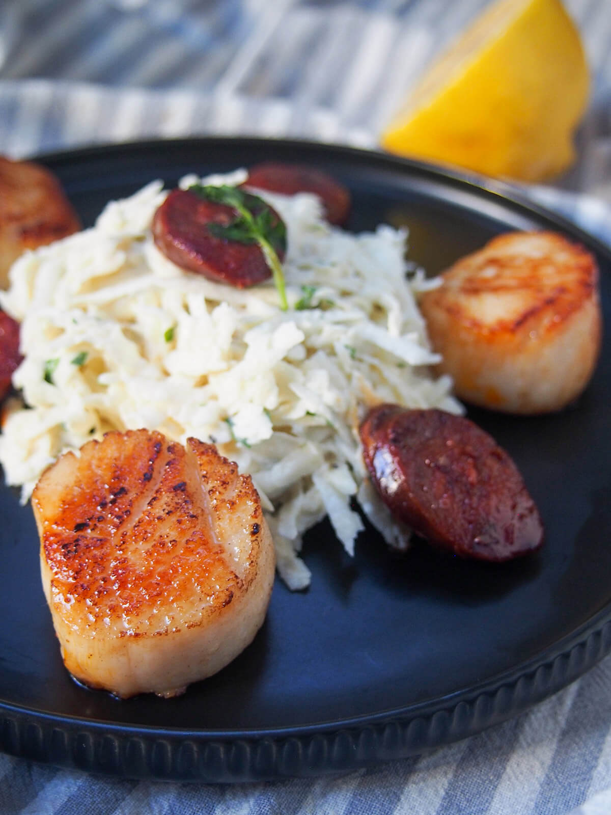 close view of seared scallop in front of mound of celeriac remoulade and slices of chorizo around