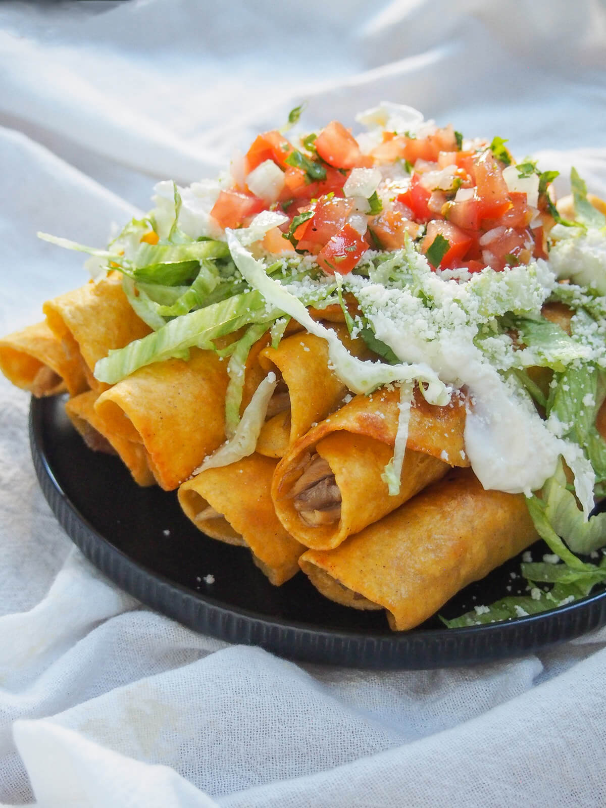 side view of plate of chicken flautas topped with lettuce and pico de gallo
