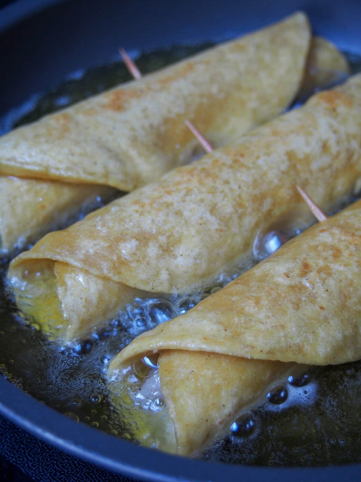 frying three chicken flautas in oil