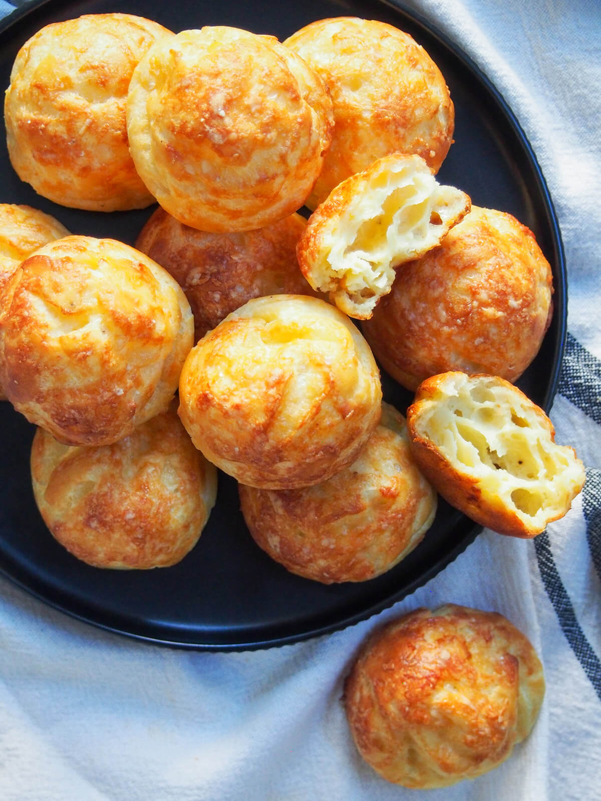 Gougères are classic French cheese puffs that make a great snack or canapé. Basically a savory choux pastry, with cheese added in, baked to crisp, light deliciousness. close overhead view of plate of gougeres cheese puffs with one split open showing airy inside