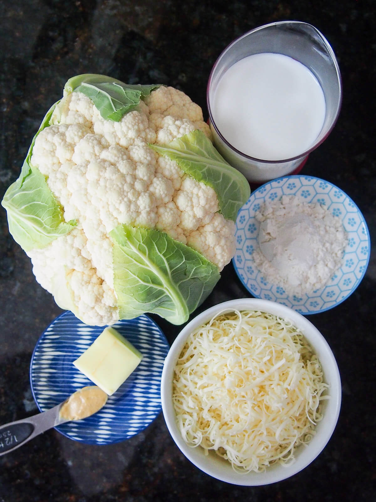 ingredients for cauliflower cheese Cauliflower, bowl of cheese, flour, milk and dish with butter and mustard