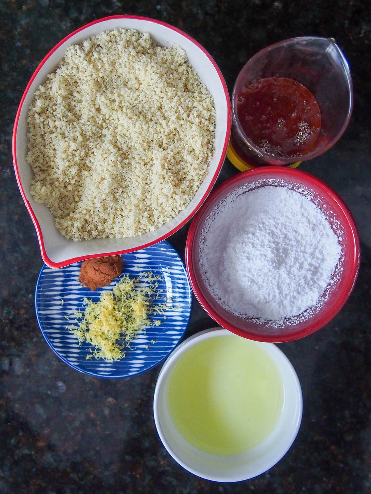 bowls with ground almonds, powdered sugar, honey, egg white and small plate with cinnamon and lemon zest