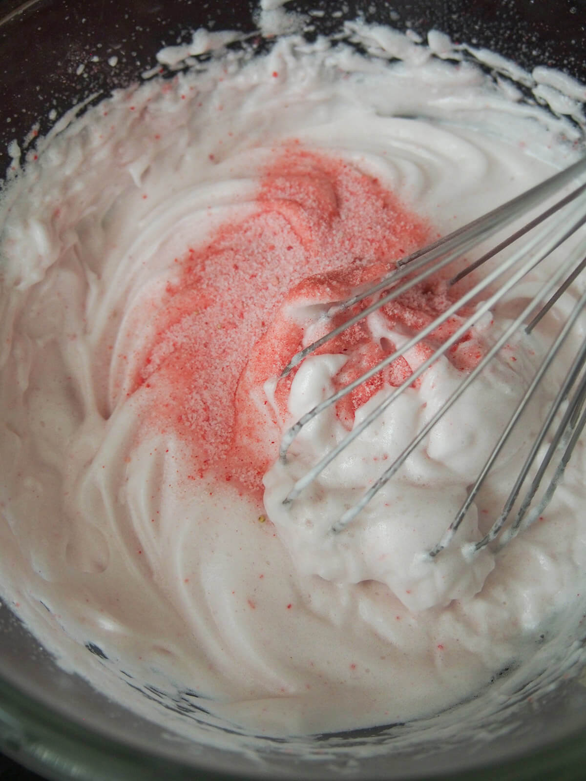 adding sugar and strawberry to whipped egg white with beater in bowl