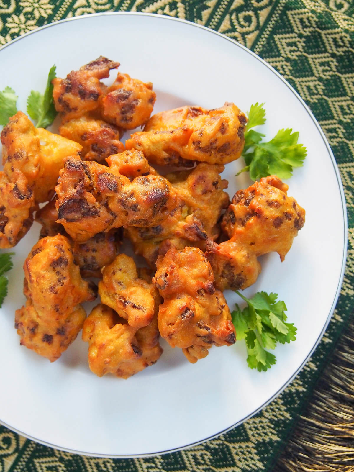 Cauliflower pakora are a traditional Indian snack or appetizer that are quick, tasty and versatile. Cook up some of these fritters to start your next Indian meal or add some to your game day or party menu! plate of cauliflower pakora from overhead