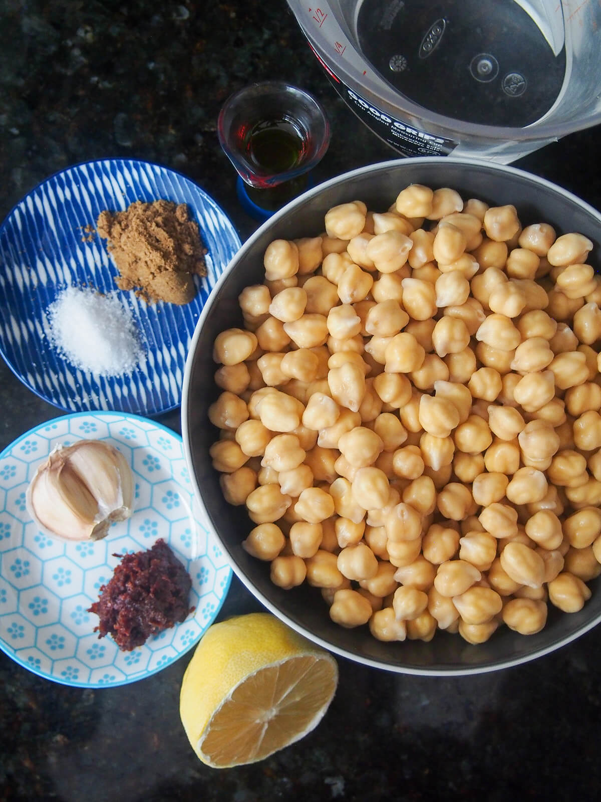 bowl of chickpeas and dishes with salt, cumin, garlic and harissa, lemon to side