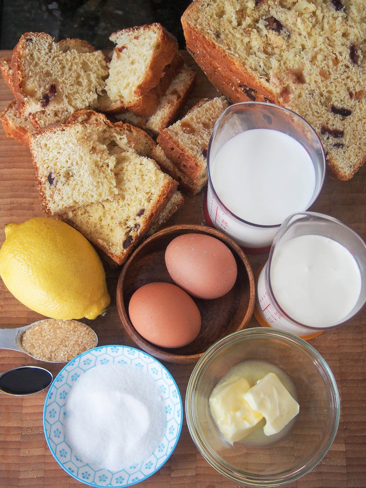 pieces of panettone, bowls with eggs, butter and sugar and measures of cream and milk on board