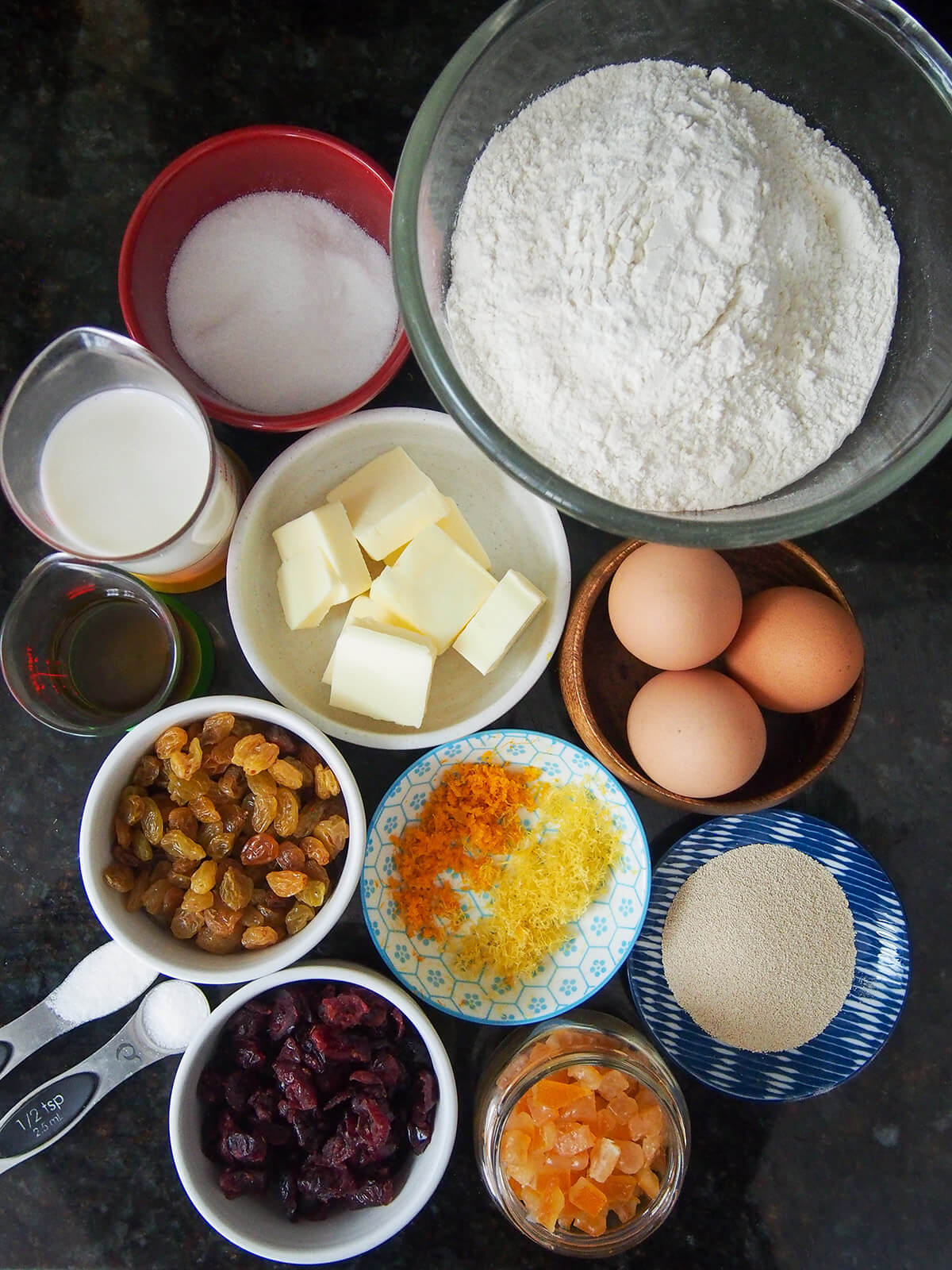 bowls with flour, sugar, eggs, dried fruit, butter, yeast and milk