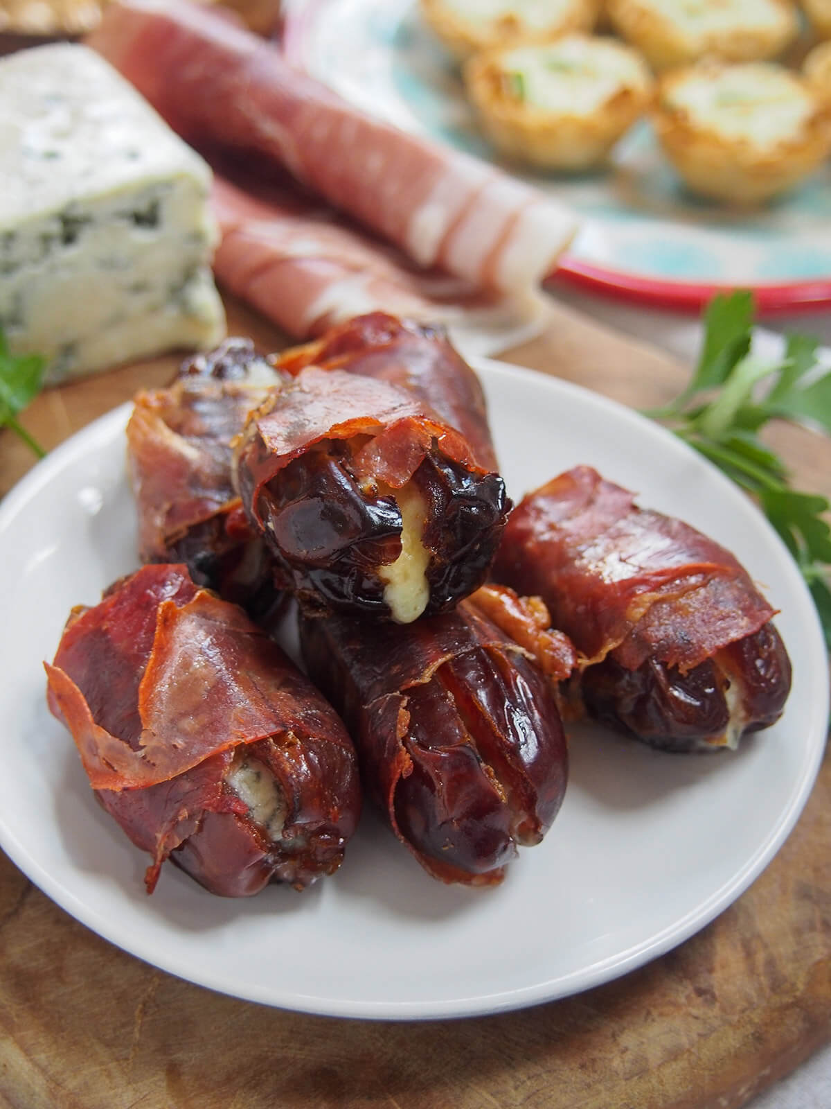 plate of prosciutto wrapped dates with cheese, ham and other appetizers behind
