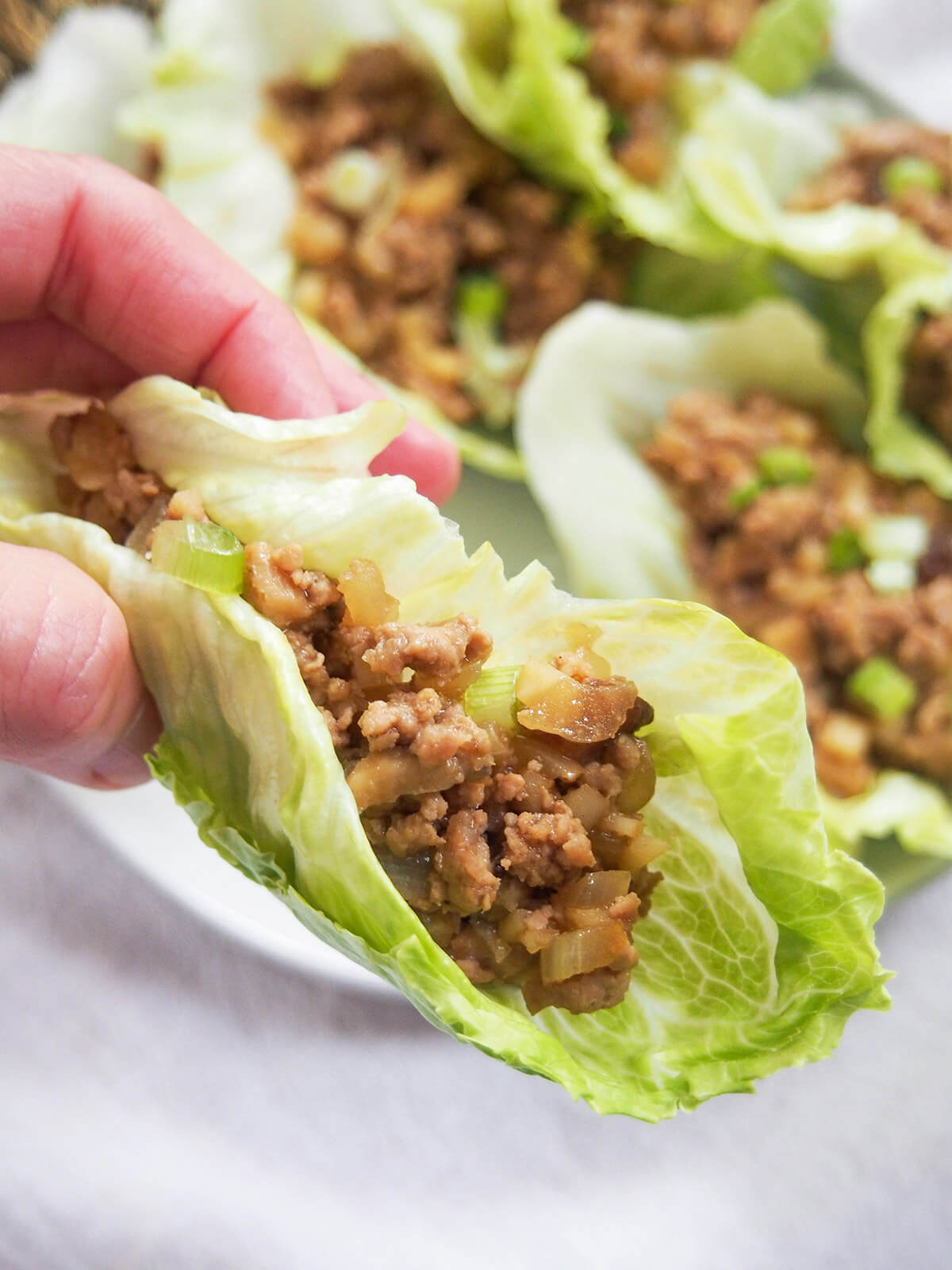 san choy bow held in hand over plate with more Chinese lettuce wraps