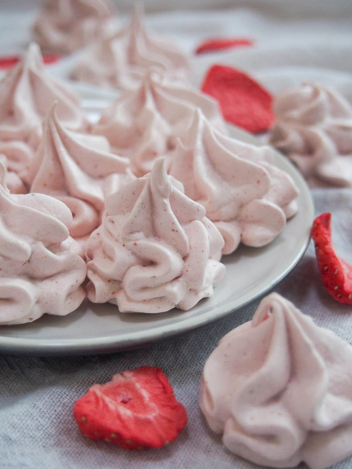 view of plate of strawberry meringue cookies from side with freeze dried strawberries around