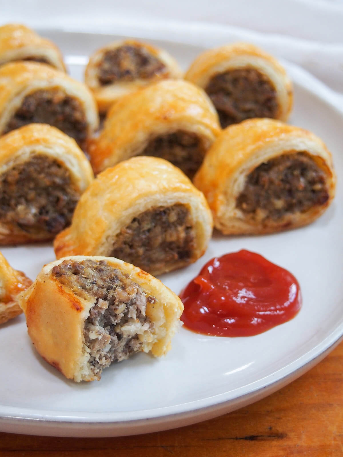 close view of haggis sausage rolls on plate with ketchup to side and one bitten roll at front