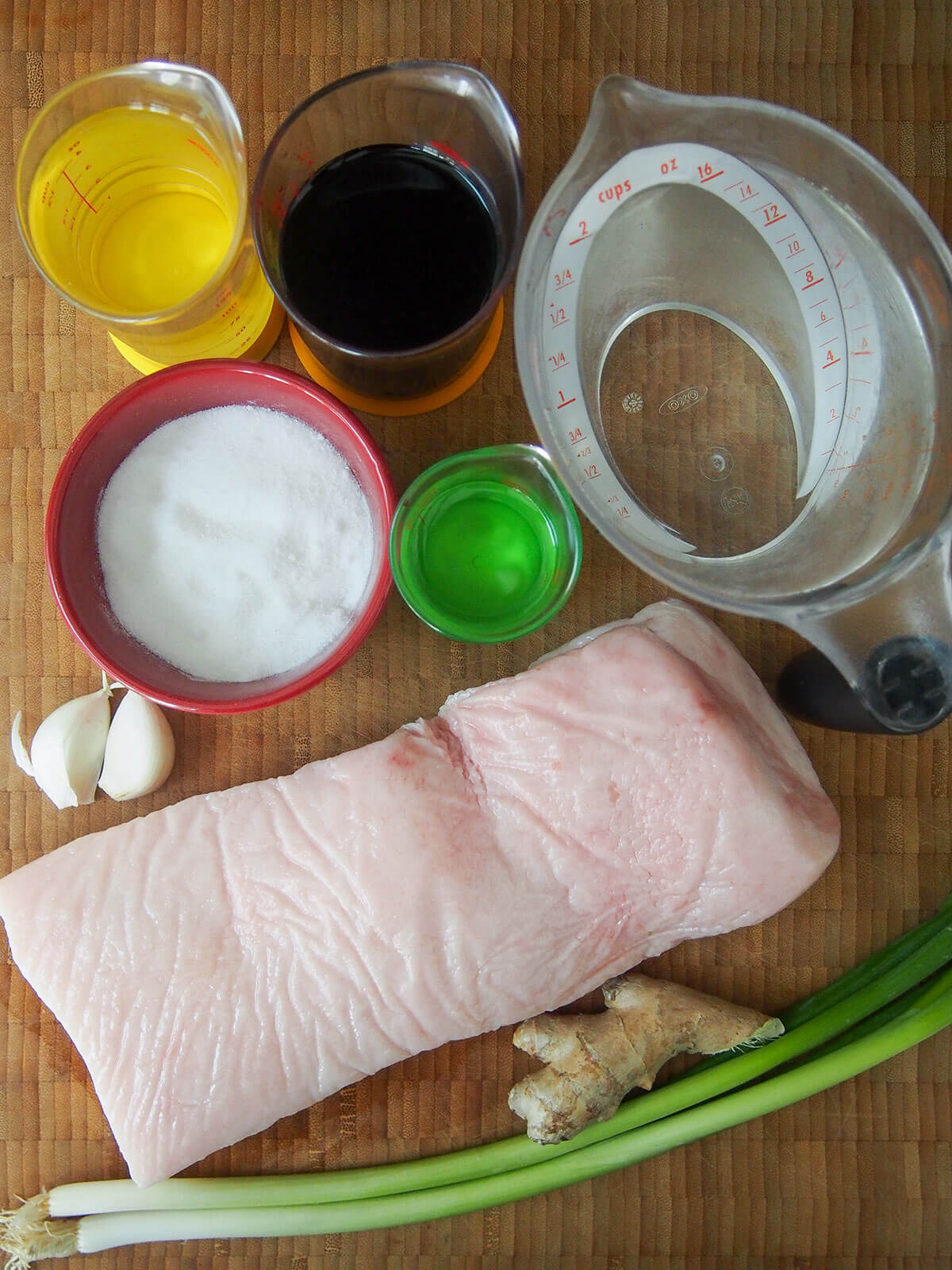 measures with water, soy, mirin, sake, bowl of sugar, piece of pork belly, ginger, garlic and green onions