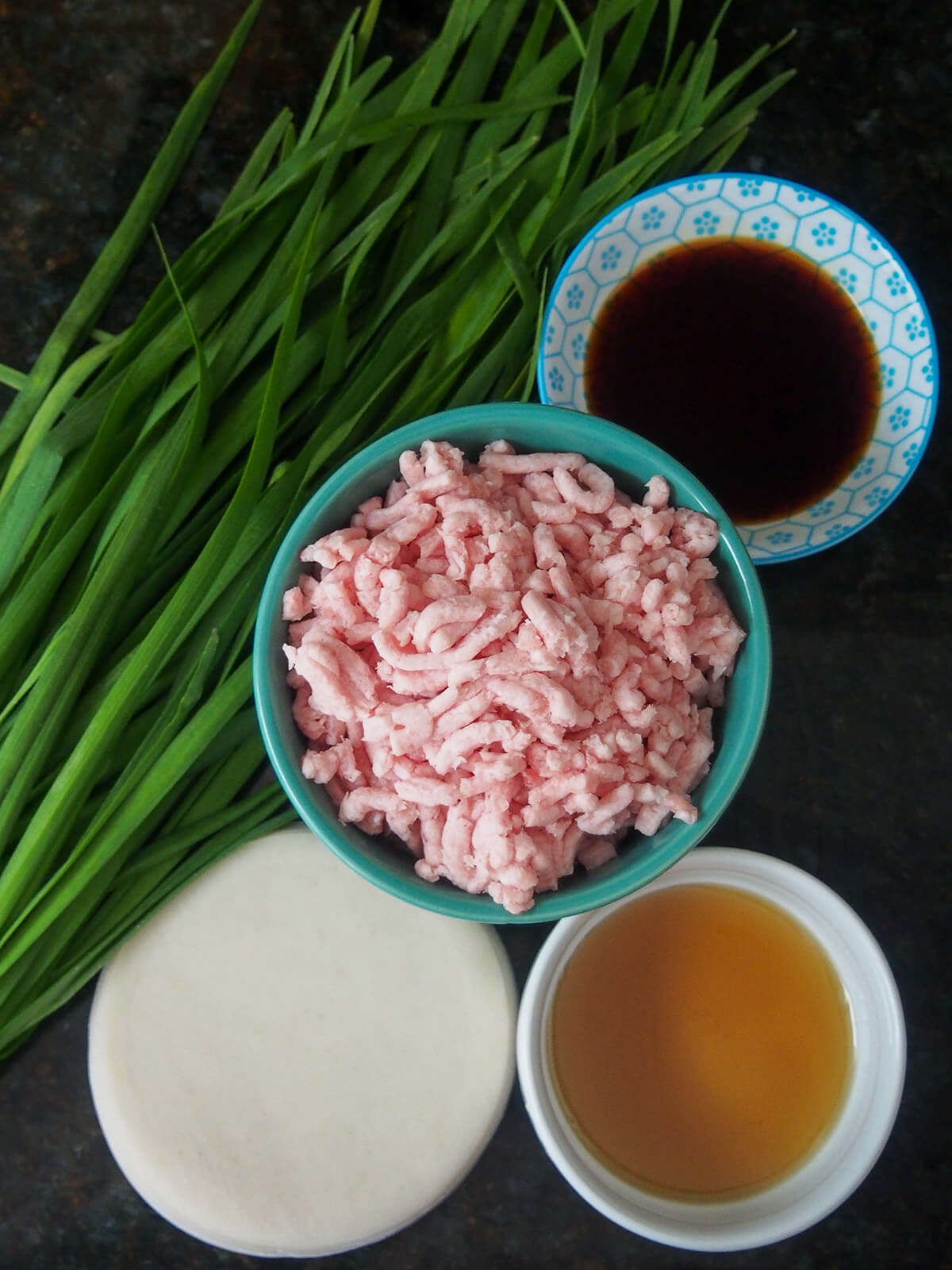 ingredients for pork and chive dumplings bowls with ground pork, soy sauce and sesame oil with dumpling wrappers and Chinese chives to side