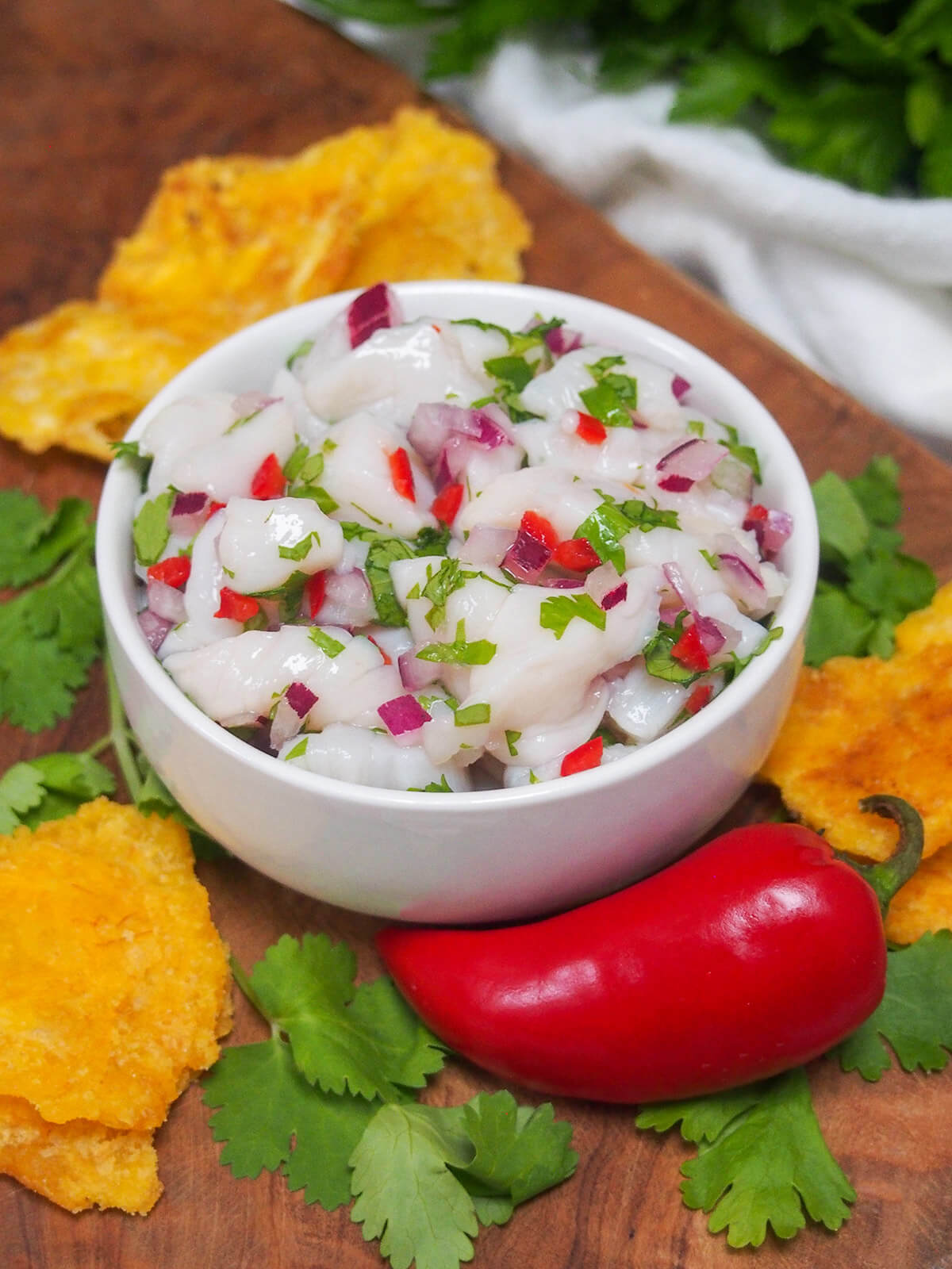 bowl of scallop ceviche with plantain chips around bowl and chili in front