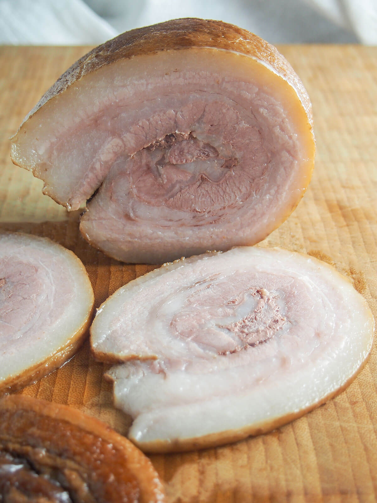 slices of chashu pork on chopping board with rolled piece at back