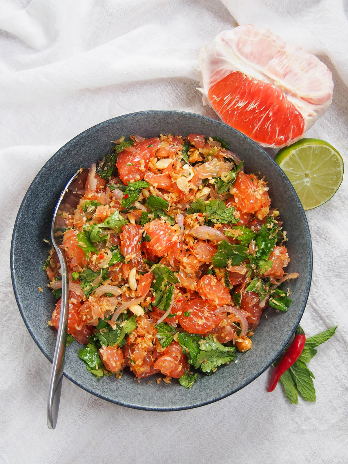 bowl of Thai pomelo salad from overhead with chunk of pomelo and lime above bowl
