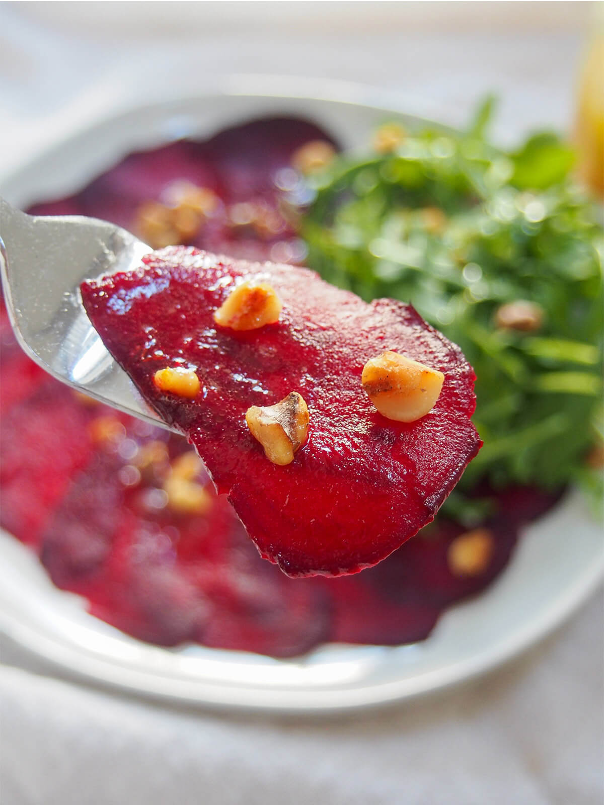 fork holding a slice of beet topped with some walnut pieces over plate