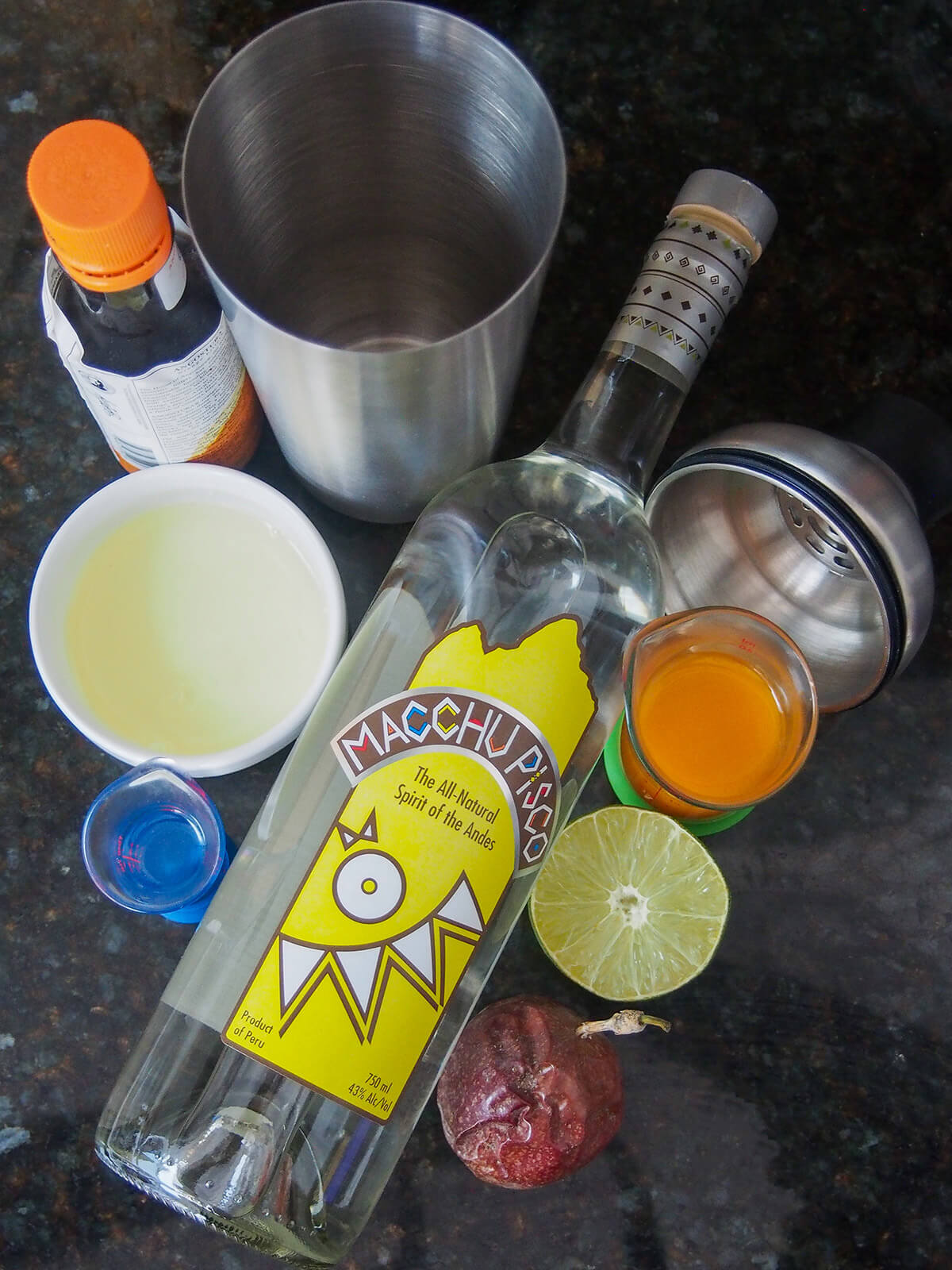 bottle of pisco and measures with egg white, passion fruit, simple syrup and lime half to side