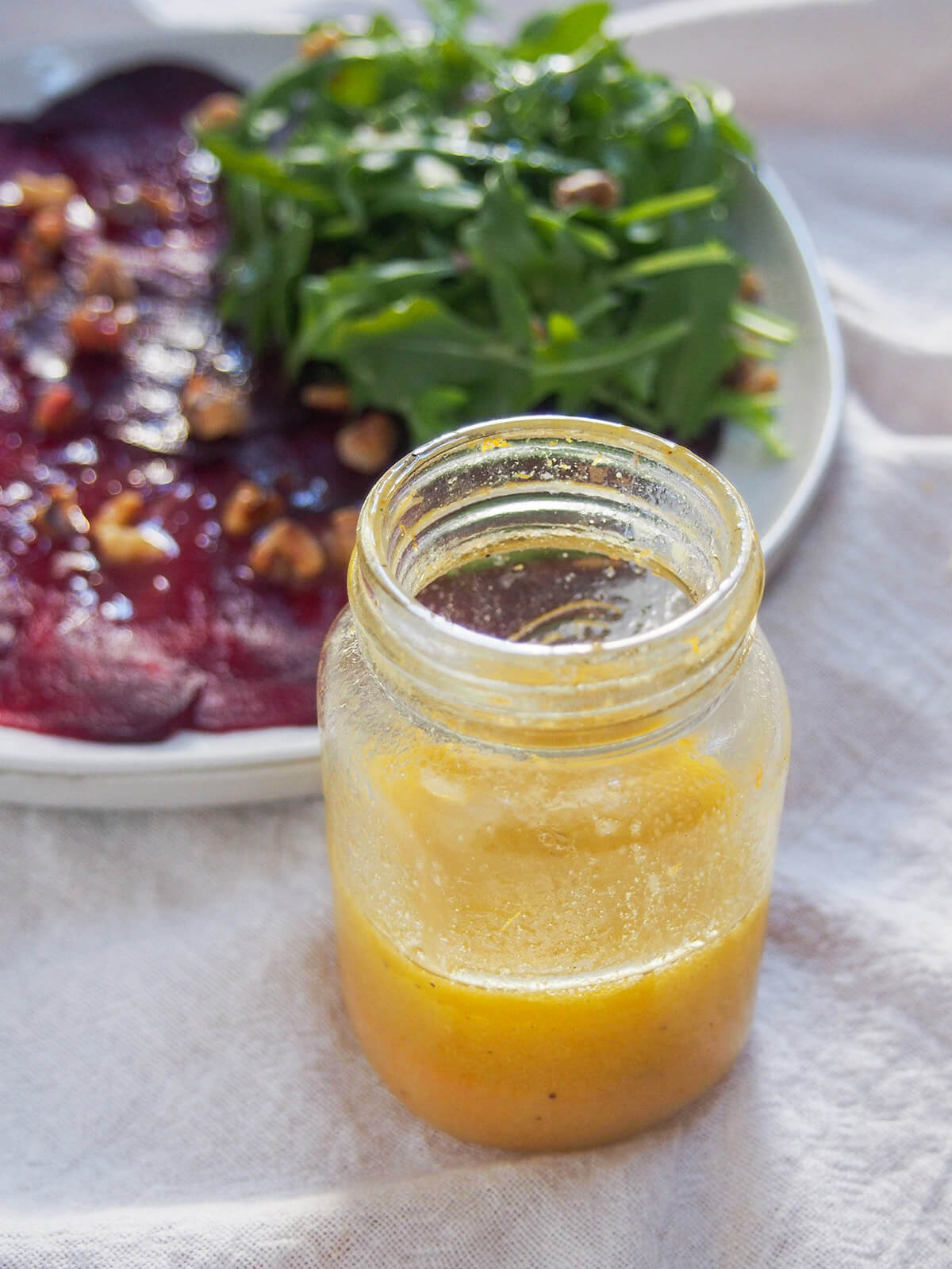 jar of orange vinaigrette in front of plate of beet carpaccio