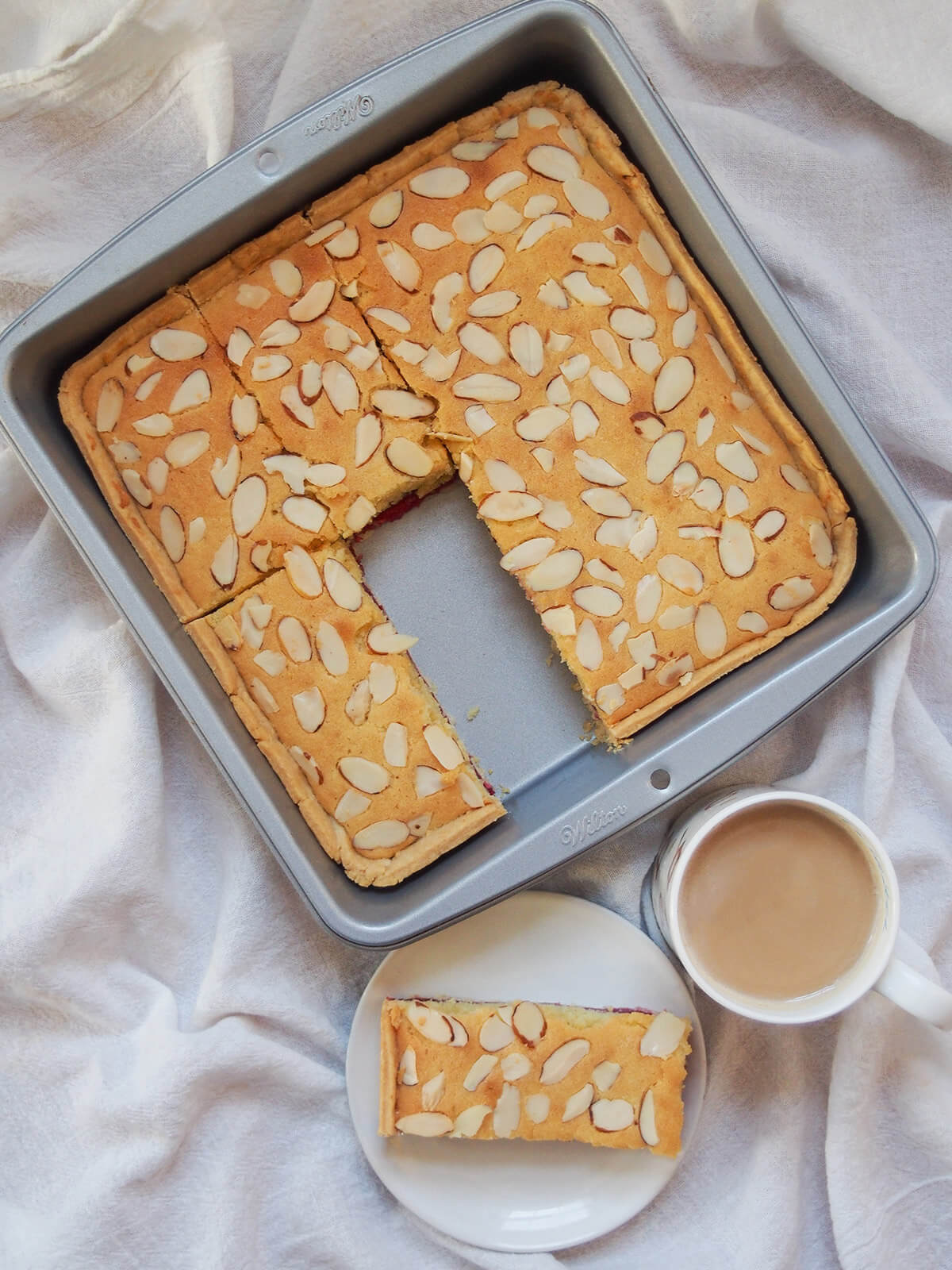 overhead view of pan of Bakewell slice with a slice on plate below
