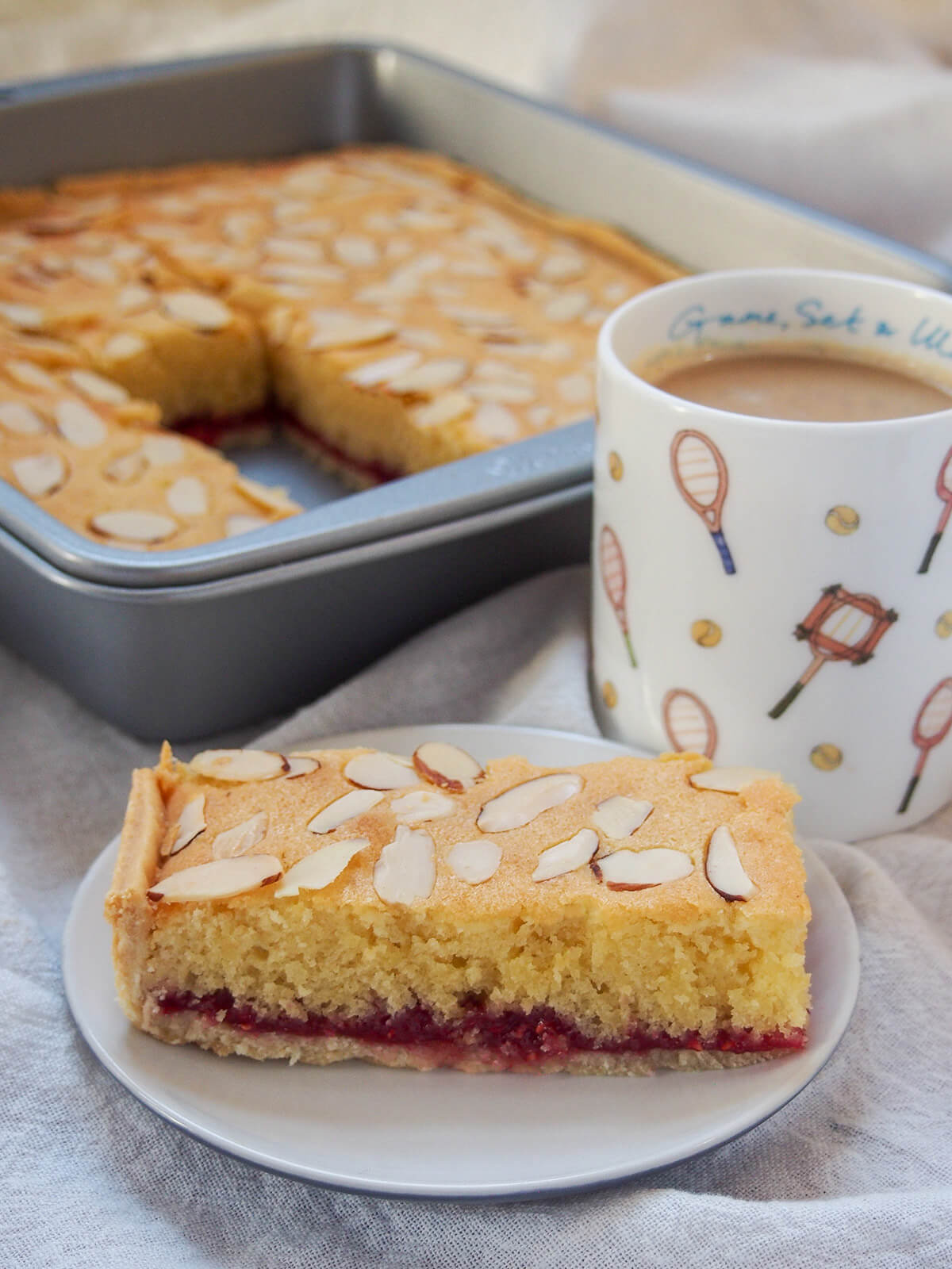 piece of Bakewell slice in front of mug and dish of rest of slice