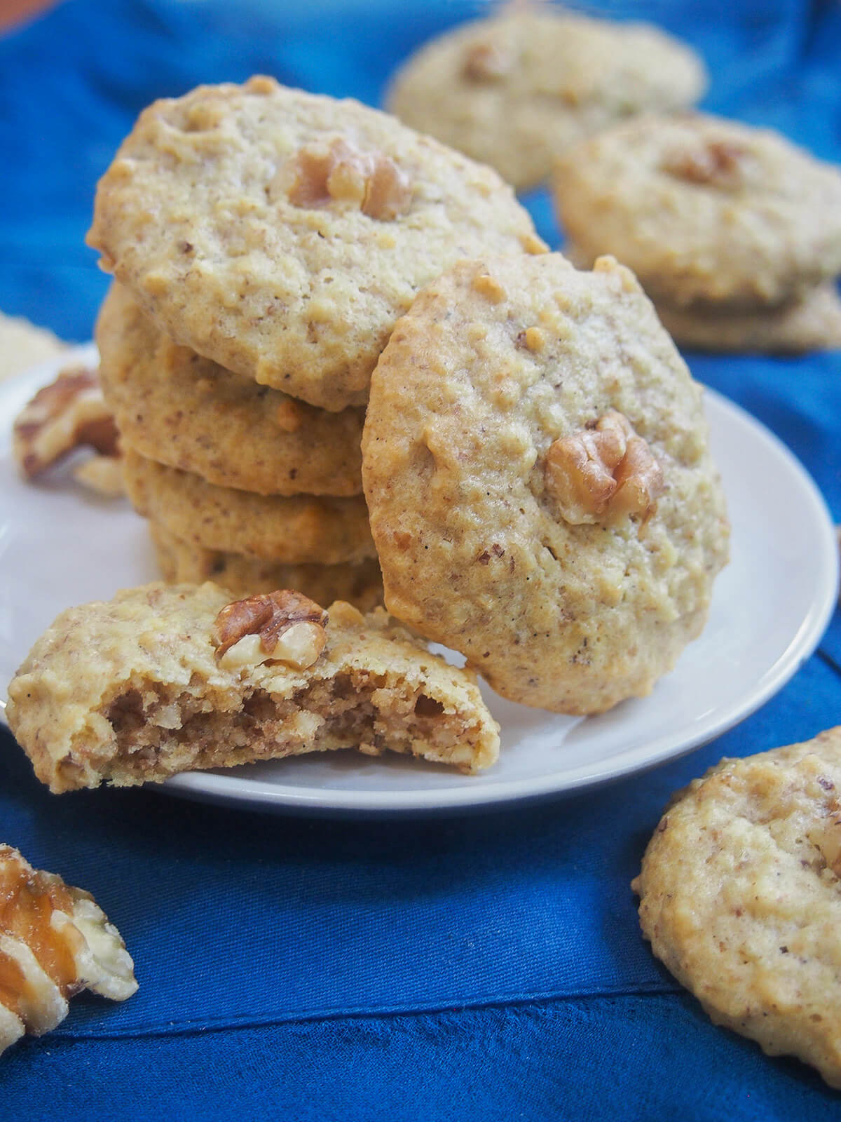These Persian walnut cookies have only four ingredients, are naturally gluten and dairy free & so easy to make. Traditionally for Nowruz, they're a tasty treat any time. stack of Persian walnut cookies with one resting to side and part cookie in front