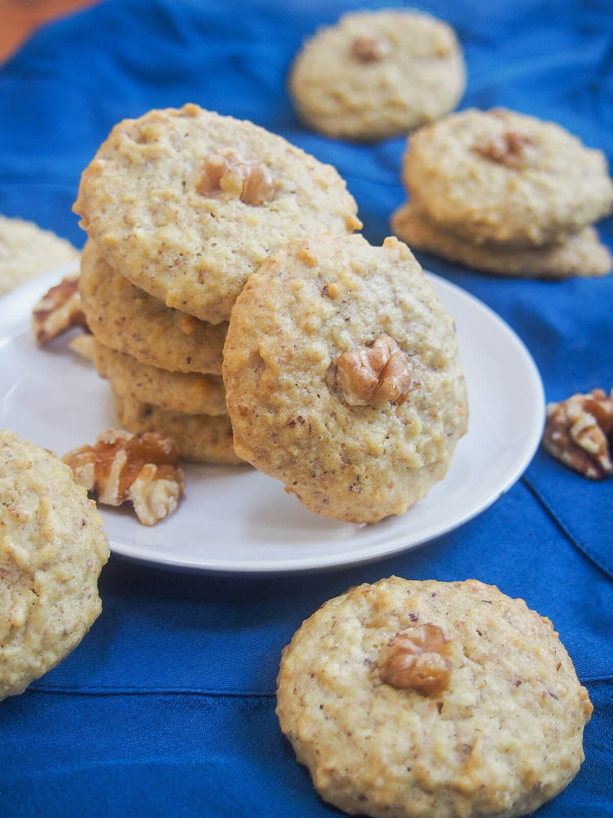 These Persian walnut cookies have only four ingredients, are naturally gluten and dairy free & so easy to make. Traditionally for Nowruz, they're a tasty treat any time. Persian walnut cookie resting on stack with more cookies in front and behind