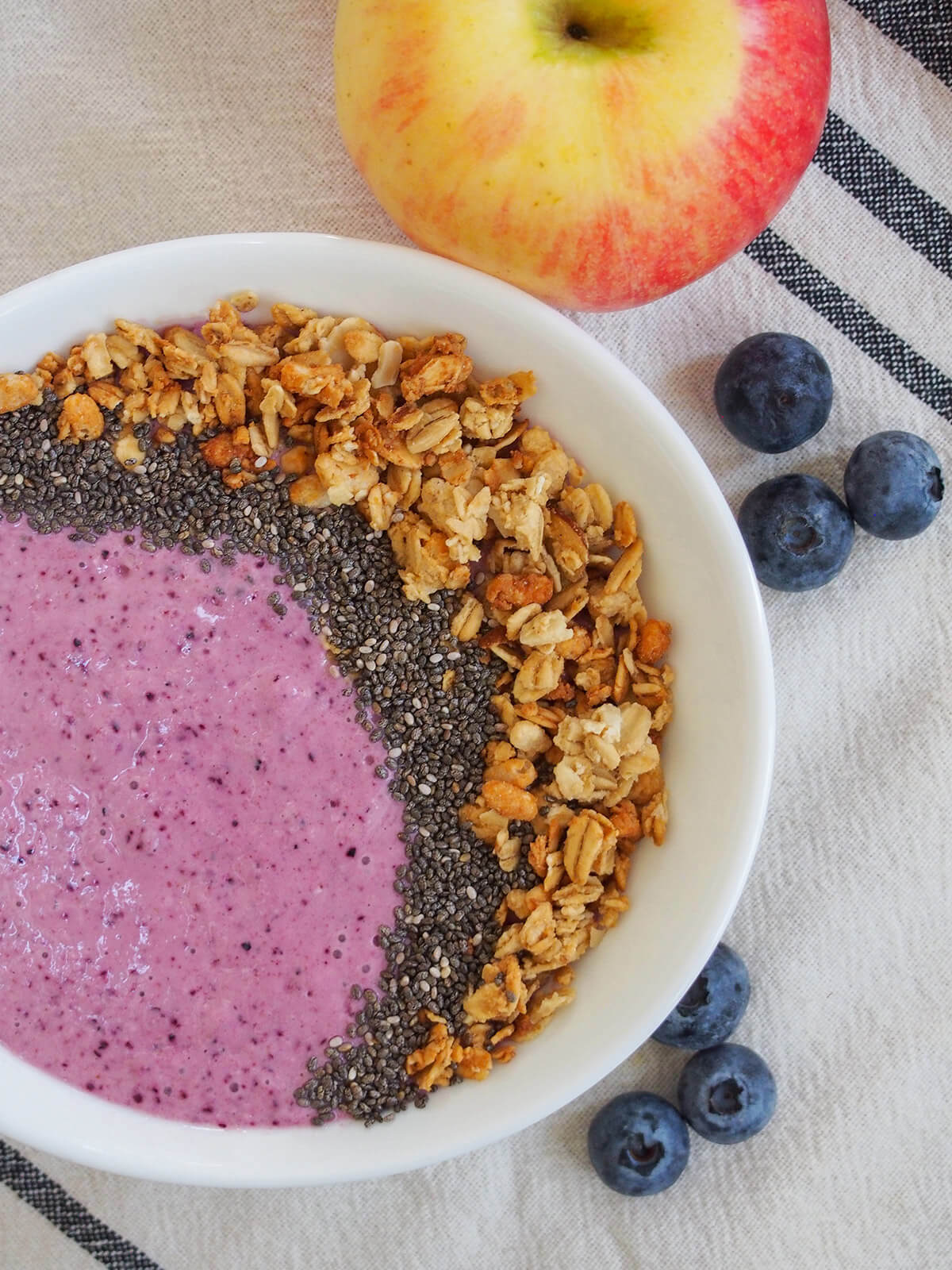 part view of bowl of blueberry apple smoothie with apple above