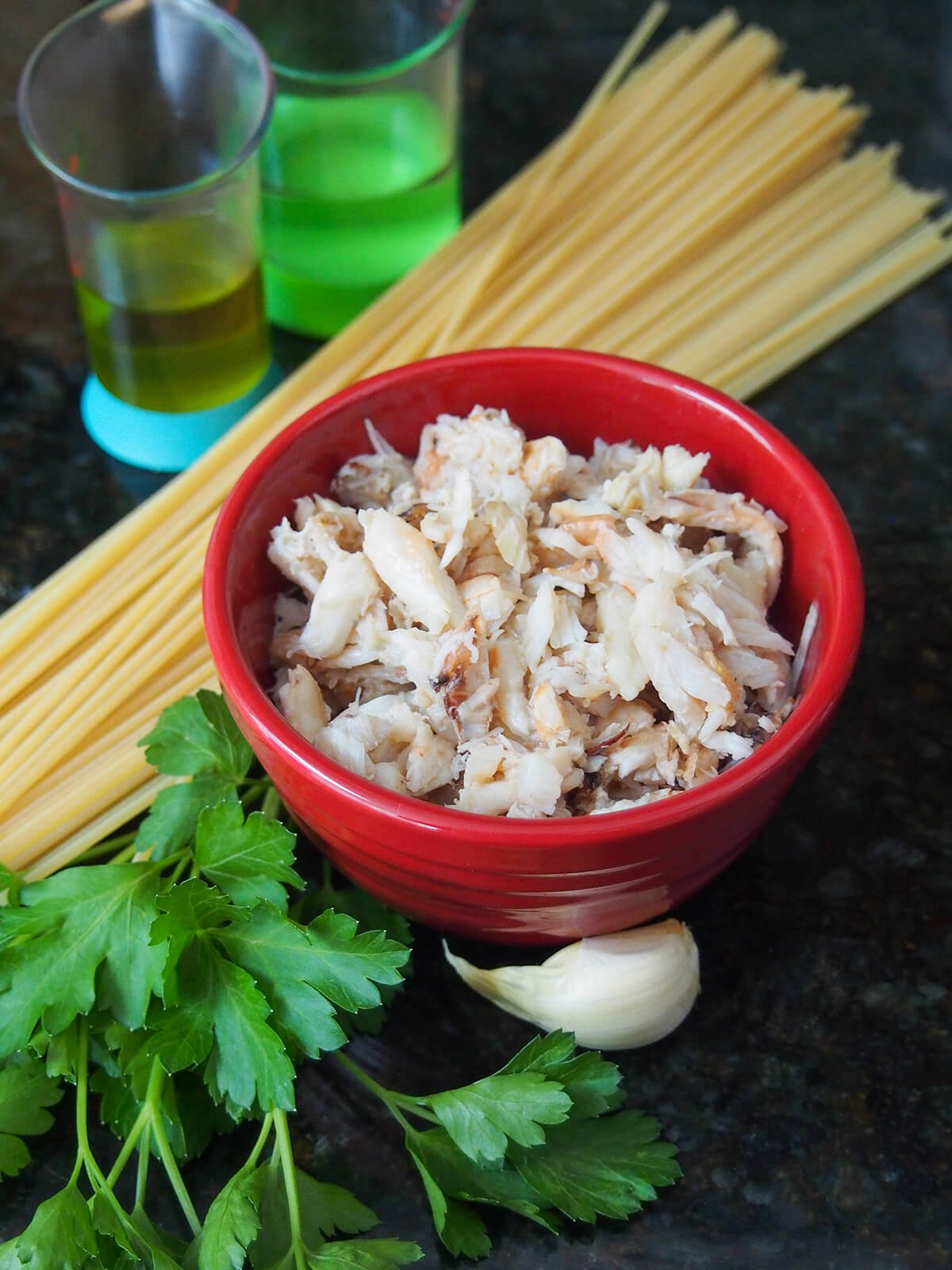 bowl of crab with spaghetti behind, garlic and parsley in front