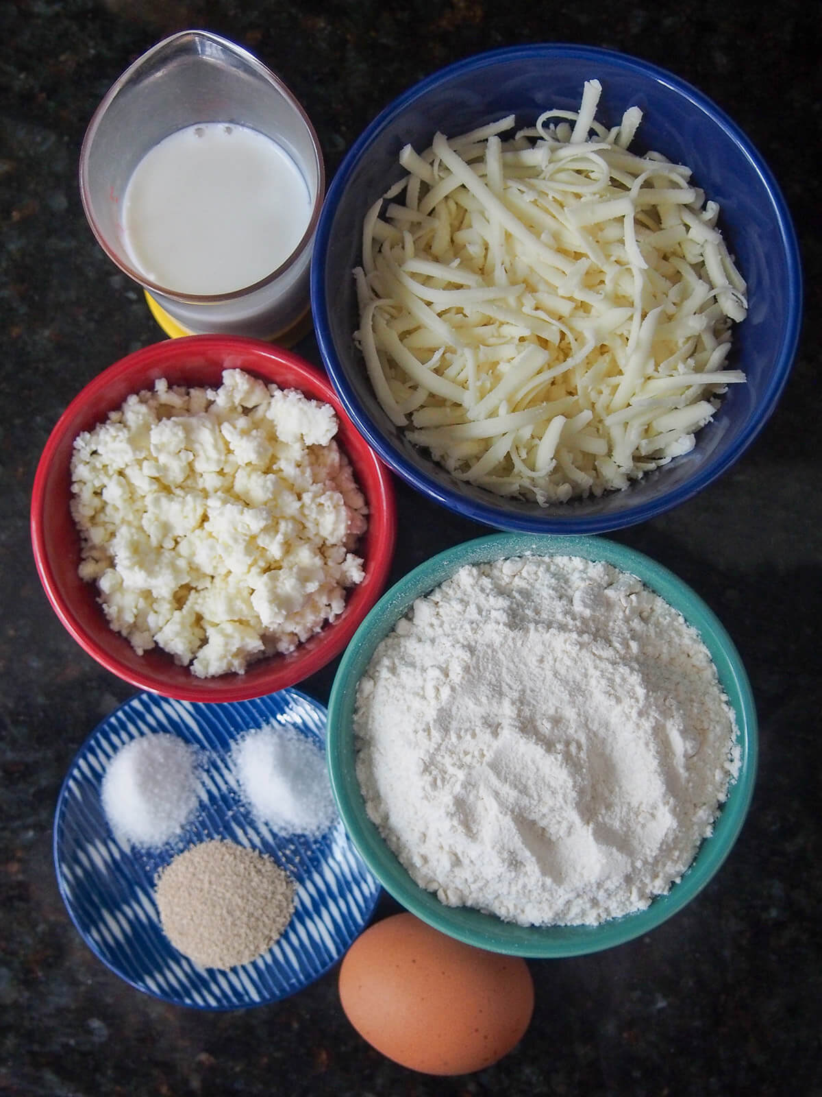 bowls with cheese, flour, milk, plate with salt, sugar and yeast and egg below