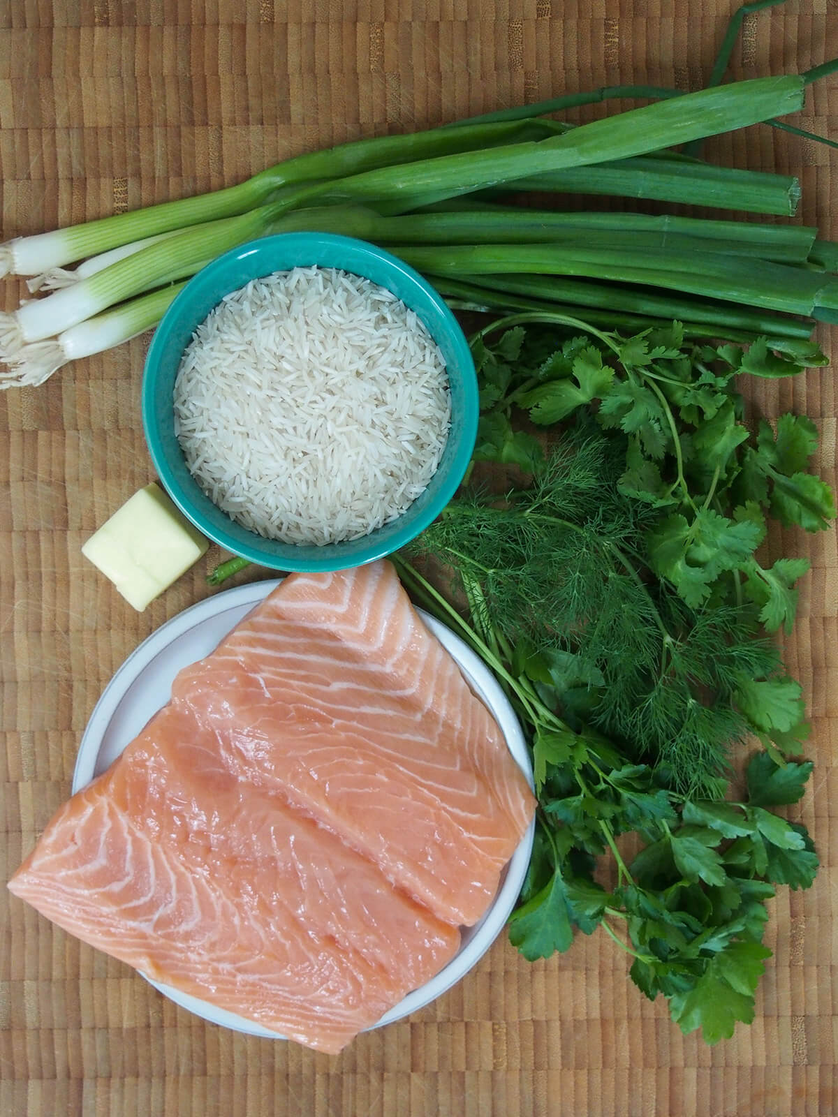 bowl of rice with herbs around and plate with salmon below