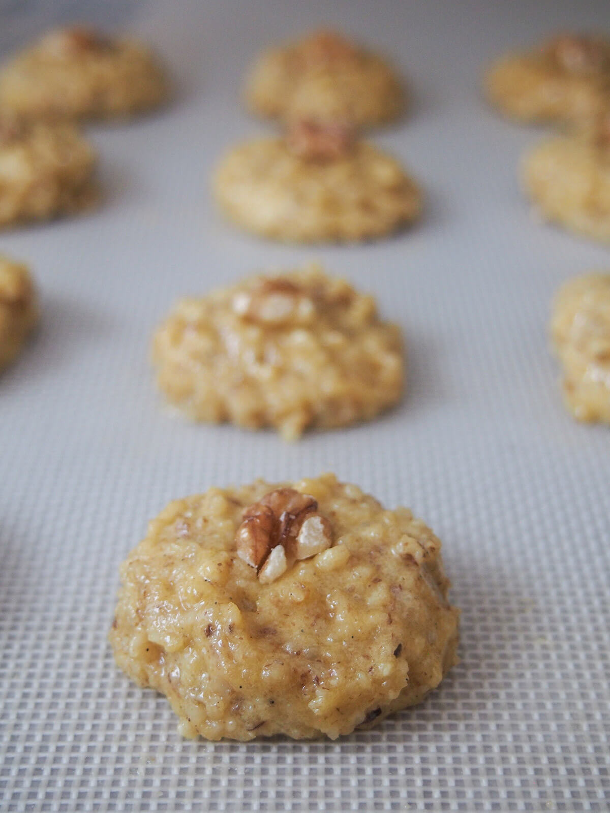 raw cookie mounds on baking sheet before baking for Persian walnut cookies raw cookie mounds topped with pieces of walnut before baking