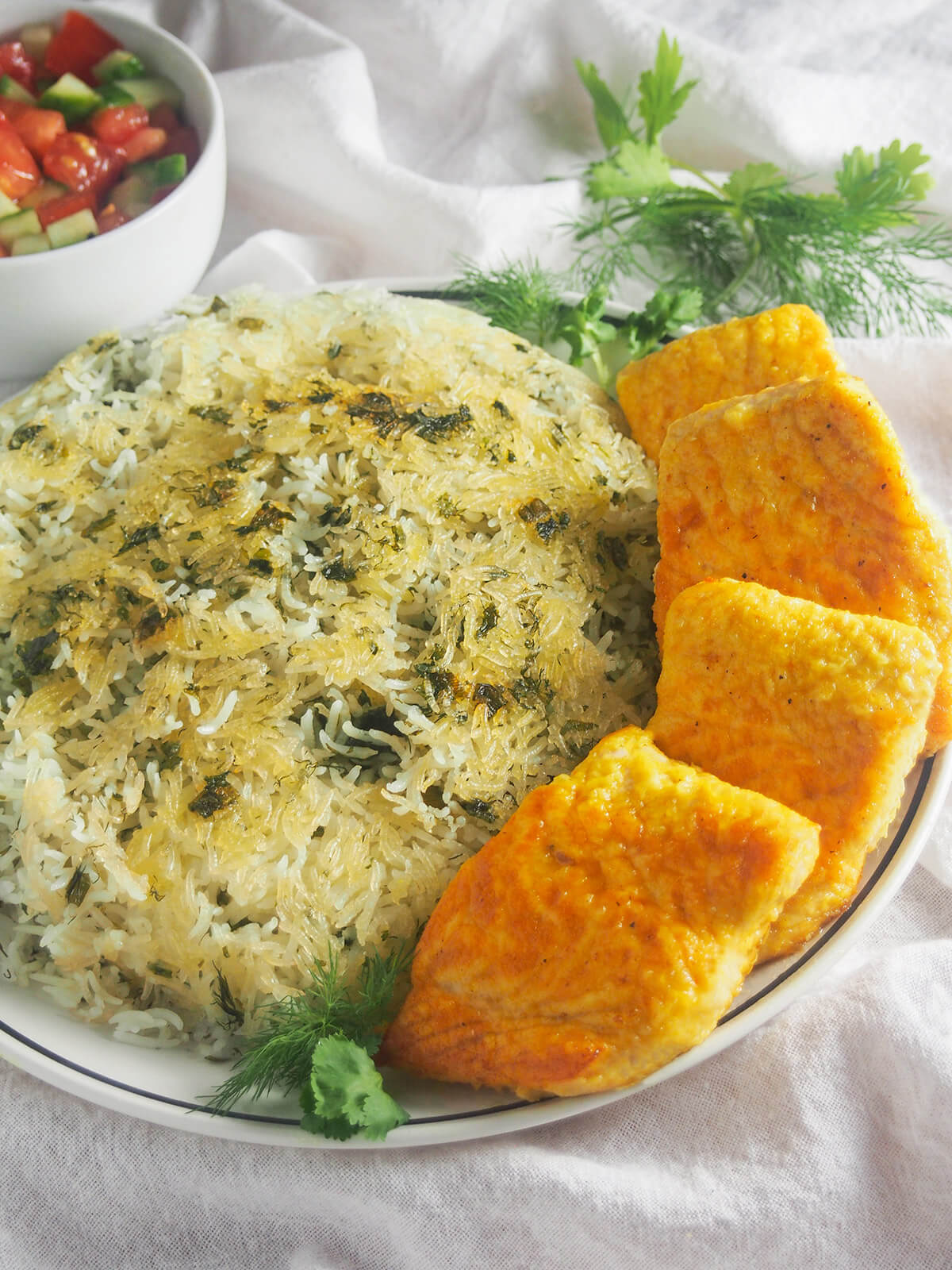 side view of Persian herb rice with fish, sabzi polo ba mahi with fish to right