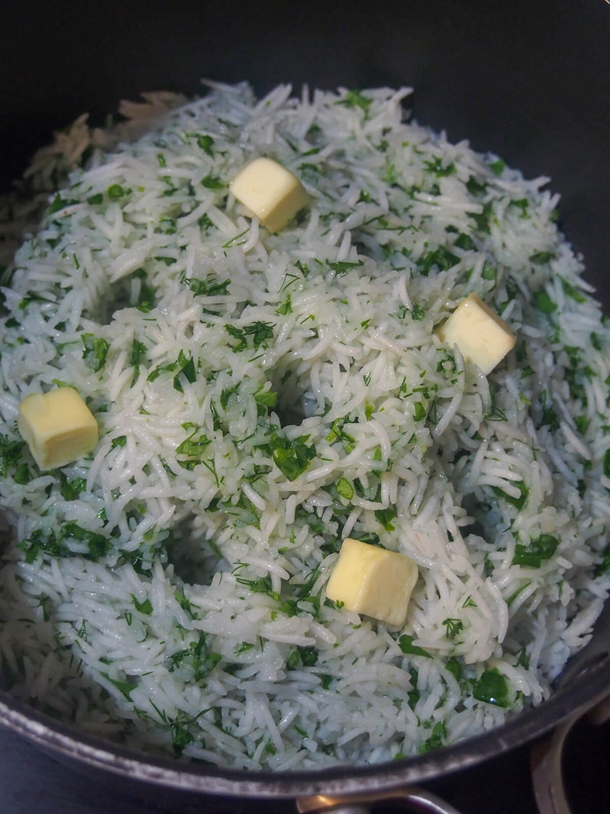 parboiled rice with herbs in pot with butter on top and holes for steam in rice