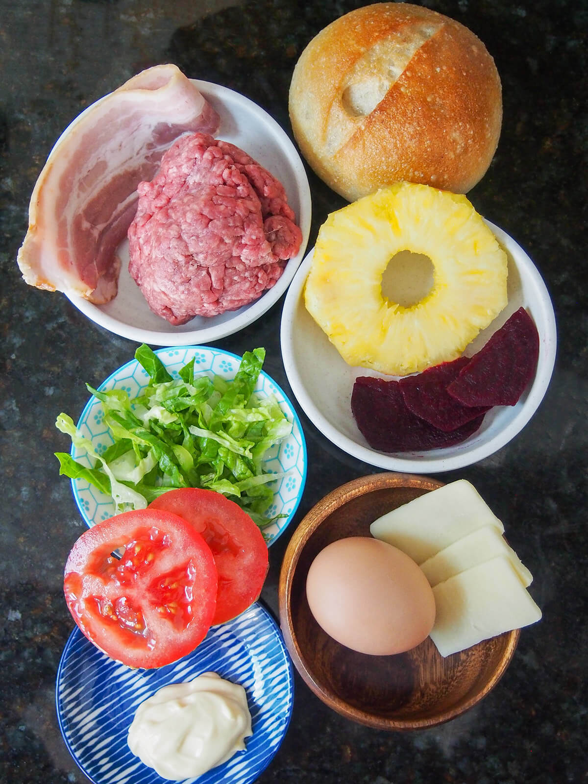 plates with ground beef, bacon, pineapple ring, beet, tomato, lettuce, egg, cheese and roll above