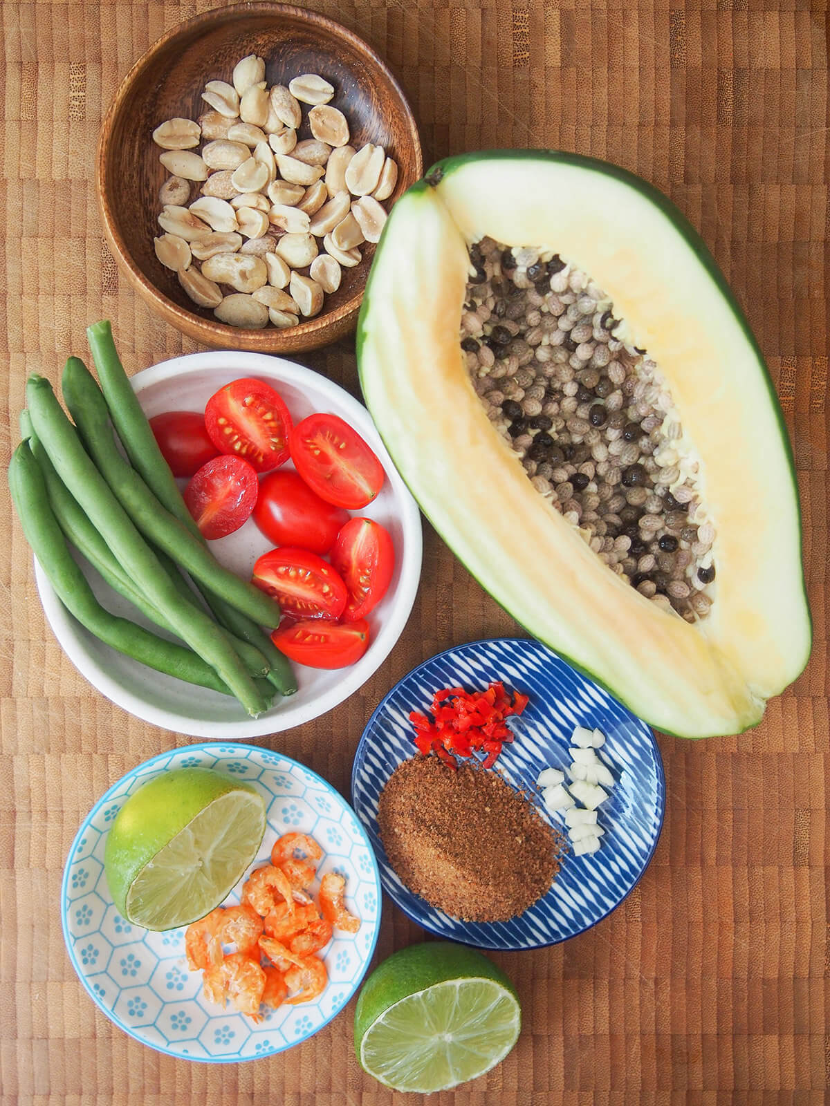 ingredients for Thai green papaya salad part of a green papaya, bowls with peanuts, tomatoes, green beans, dried shrimp and lime