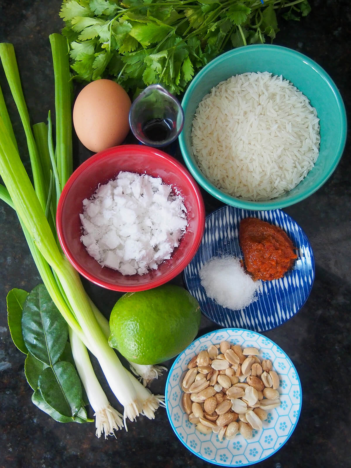 bowls with rice, coconut, peanuts, curry paste with lime, egg, scallions, cilantro and lime leaves to side