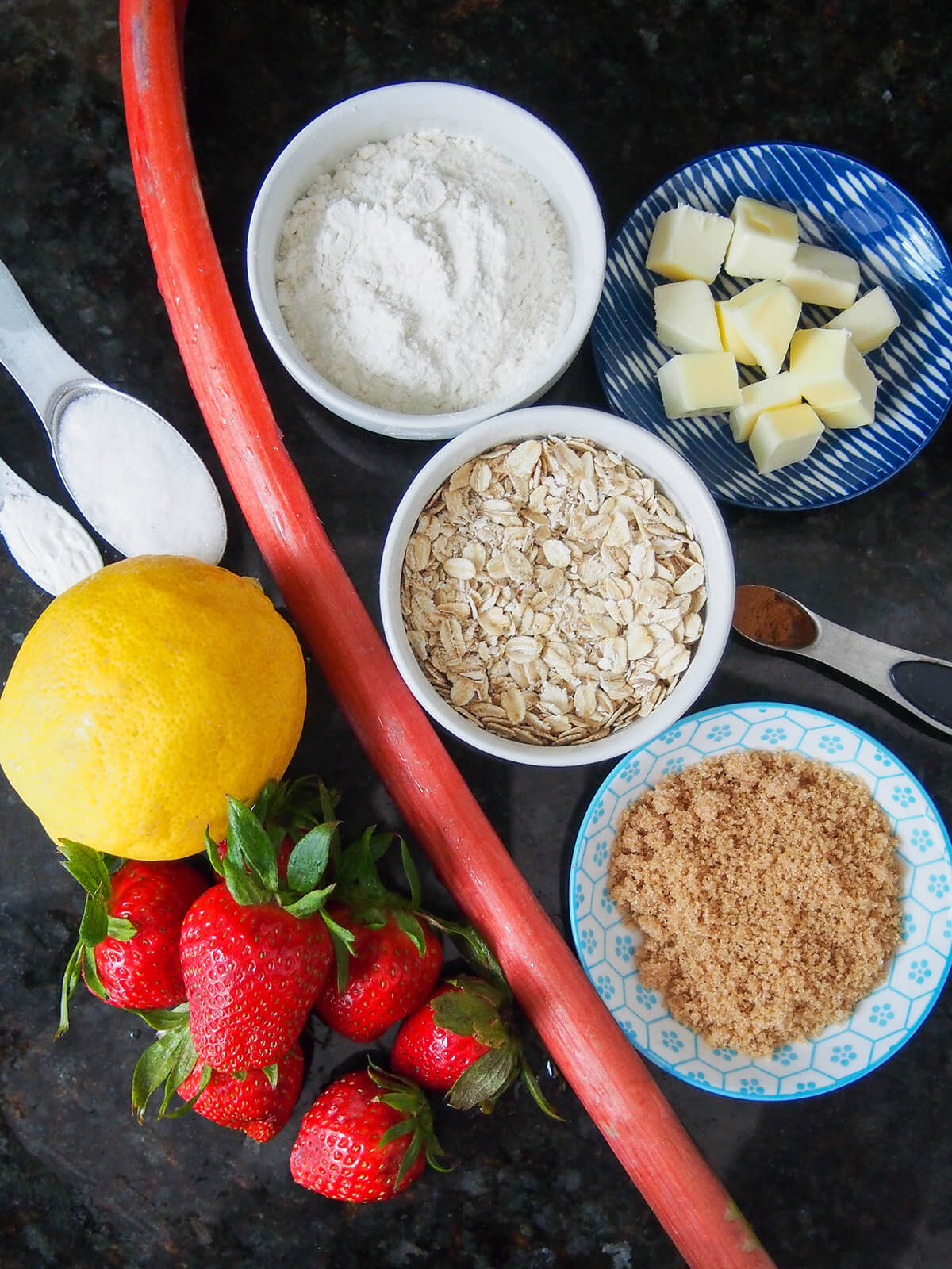 ingredients for strawberry rhubarb crisp from overhead bowls with flour, oats, sugar and butter with strawberries, lemon and rhubarb on side