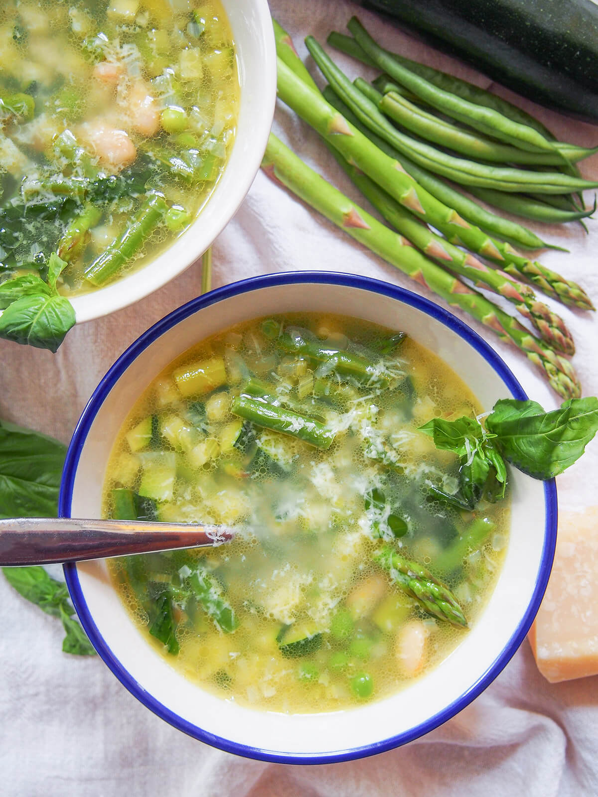 Minestrone primavera is a wonderful bowlful of spring flavors, with plenty green vegetables, white beans and a light stock base. Easy to make, adaptable & perfect on cooler spring days. bowl of minestrone primavera with vegetables above and part of other bowl showing