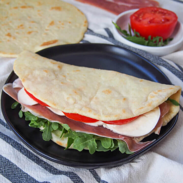 filled and folded piadina Italian flatbread on plate with tomato and additional un-filled flatbread behind