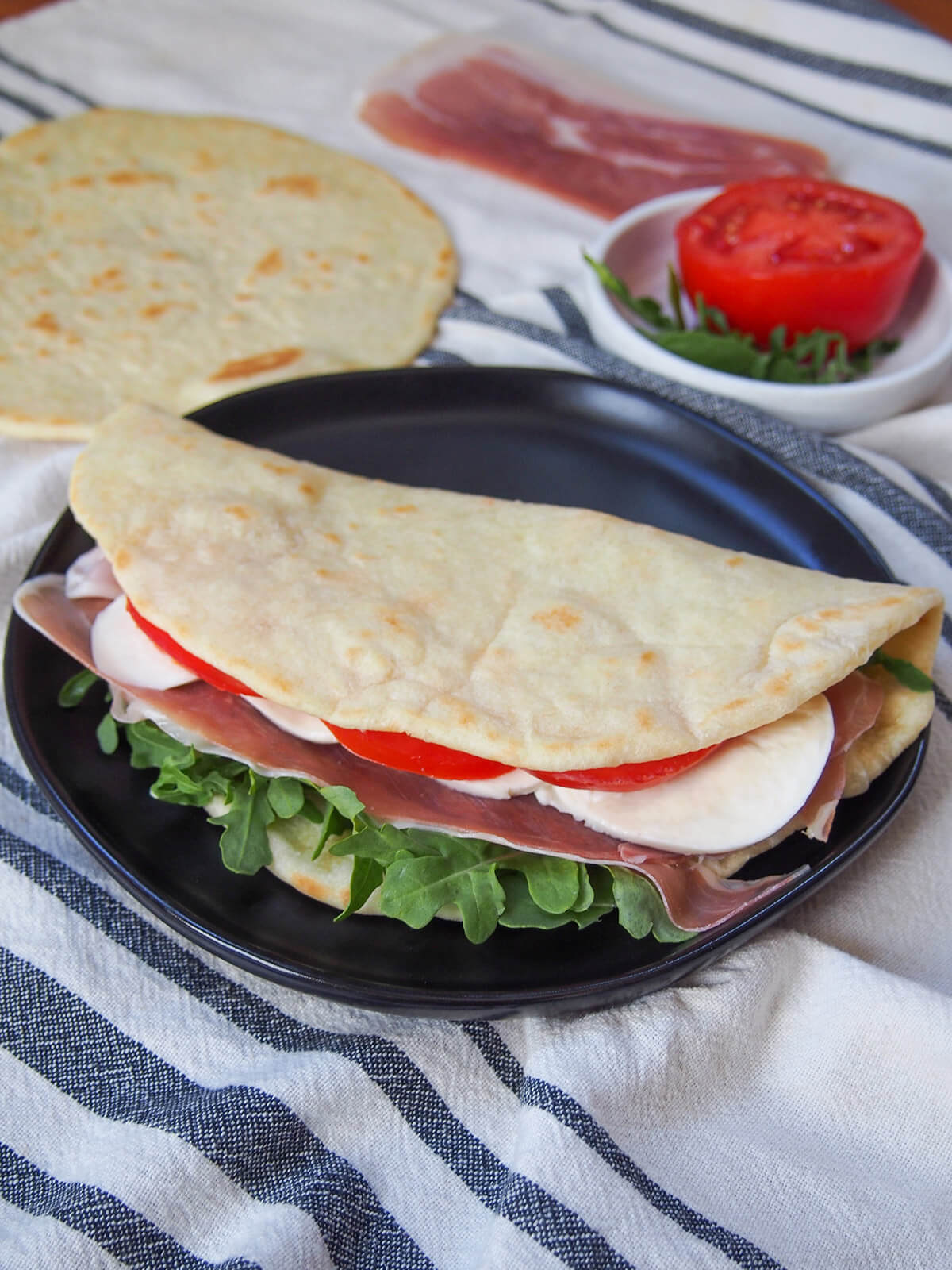 piadina with fillings on plate with another flatbread behind and dish with tomato