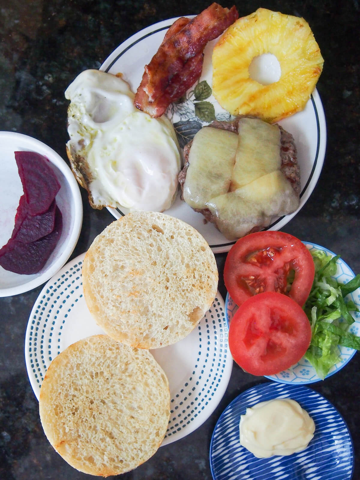 cheeseburger, egg, bun, bacon and other ingredients ready to assemble