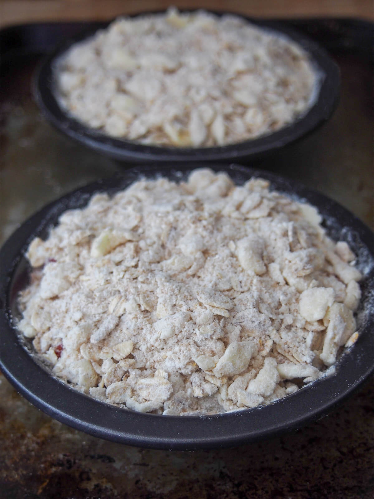 strawberry rhubarb crisp before baking oat and flout topping over fruit in small pie dishes before baking
