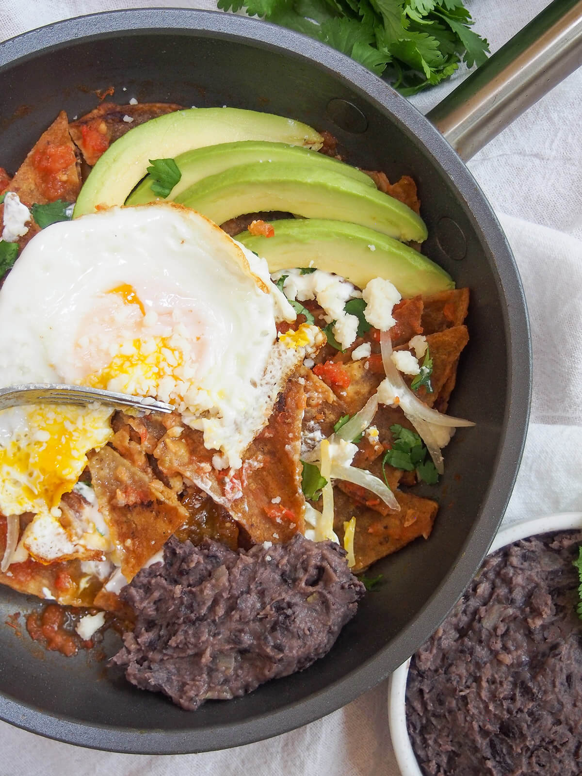 some refried black beans in skillet of chilaquiles, topped with egg and avocado