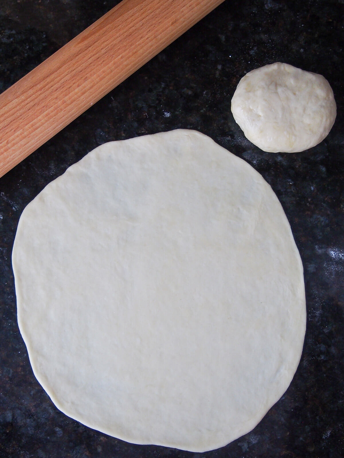 piadina rolled out in very thin circle with dough for another to one side and rolling pin to other side